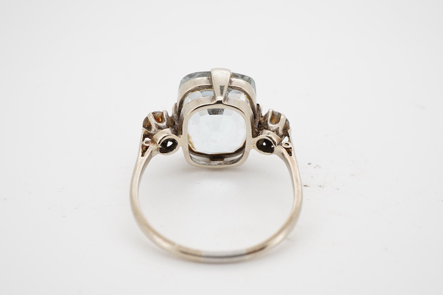 A mid 20th century white metal and single stone cushion cut blue topaz set dress ring, with two stone topaz set shoulders, size R.